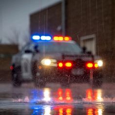 two police cars parked on the side of the road with their lights on in the rain