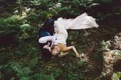 a bride and groom laying on the ground in some ferns with their arms around each other