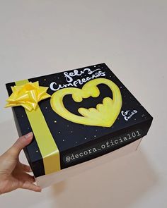 a hand holding a batman themed box with yellow ribbon and bow on it's side