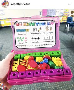 a child's hand holding a pink toy case filled with lots of colorful toys