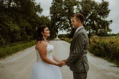 a bride and groom standing in the middle of a dirt road holding each other's hands