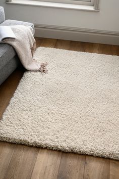 a large white rug on the floor in front of a window with a couch and chair