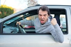 a man in a hoodie driving a car with his hand on the steering wheel