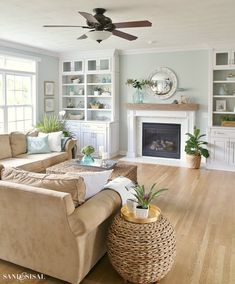 a living room filled with furniture and a fire place under a ceiling fan on top of a hard wood floor