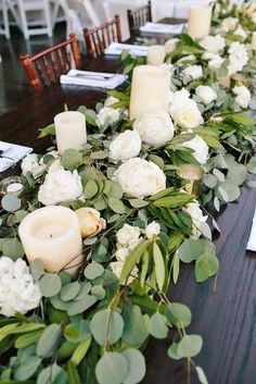 the table is set with candles and flowers on it, along with greenery for decoration