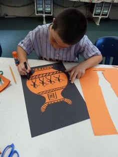 a young boy sitting at a table with scissors and paper cut out to look like an orange vase