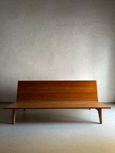 a wooden bench sitting on top of a white floor in front of a gray wall