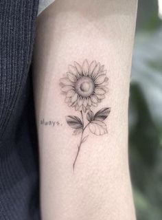 a sunflower tattoo on the arm with words written in cursive writing below it