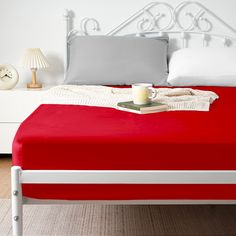 a red bed with white headboard and pillows on top of it, next to a lamp