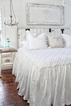 a white bed with ruffled bedspread and pillows on it in a bedroom