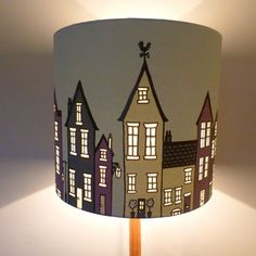 a lamp that is sitting on top of a table next to a white wall with houses painted on it