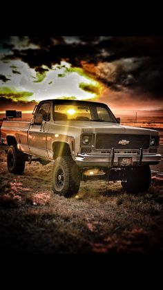 an old pickup truck parked in a field with the sun shining through clouds above it