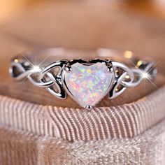 an opal heart shaped ring on top of a cloth covered box with three diamonds