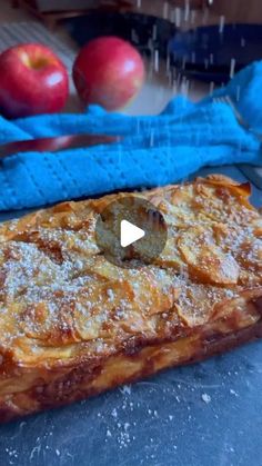 an apple tart sitting on top of a table next to two apples and a blue cloth