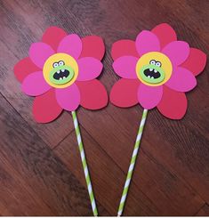 two paper flowers with faces on them sitting on a wooden floor next to straws