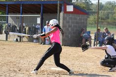 a woman swinging a bat at a ball during a softball game on a dirt field