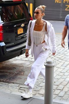 a woman in white is walking down the street with a man wearing sunglasses and a jacket