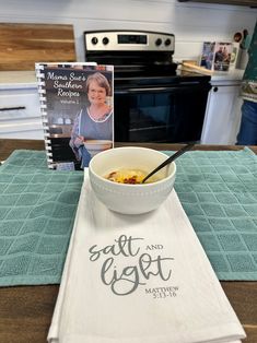 a bowl of soup sits on a kitchen table next to a cookbook