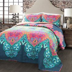 a bed with a colorful comforter on top of it next to a brick wall