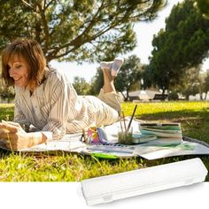 a woman laying on the grass with her laptop and books in front of her, reading