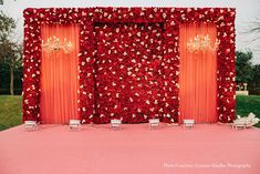 an outdoor ceremony setup with red and gold flowers on the wall, chandeliers hanging from the ceiling