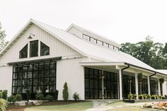 a large white barn with lots of windows and plants on the front lawn in front of it