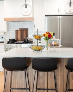 a kitchen island with three bar stools in front of it and flowers on the counter