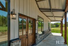 the front porch of a building with two doors and windows on each side, overlooking a grassy field