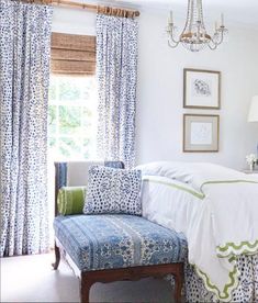 a bedroom with blue and white bedding, chandelier, window curtains, and a bench