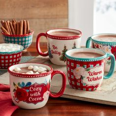 four mugs filled with hot chocolate and marshmallows sit on a tray