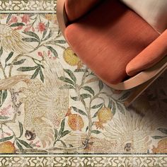 an orange chair sitting on top of a floor next to a rug with flowers and birds