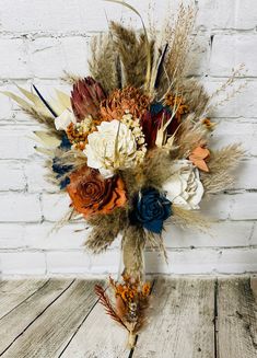 an arrangement of dried flowers and feathers on a wooden table next to a brick wall