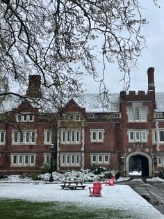 a red chair sitting in front of a building covered in snow next to a tree