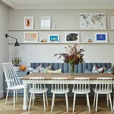 a dining room table with white chairs and pictures on the wall