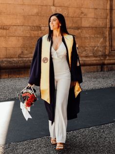 a woman is walking down the street with flowers in her hand and wearing a graduation robe