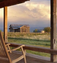 a wooden bench sitting on top of a wooden porch next to a house in the distance