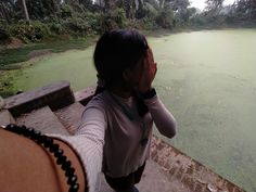 a woman standing on top of a wooden bridge next to a body of green water