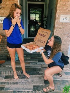 two girls are eating pizza outside on the front steps and one girl is holding a box