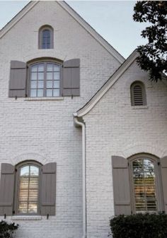 a large white brick house with shutters open and two windows on each side of the house