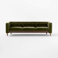 a green velvet couch with wooden legs on a white background in front of a wall