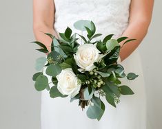 a bride holding a bouquet of white roses and greenery