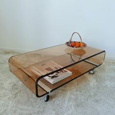 a coffee table with a basket of fruit on top and magazines under the glass shelf