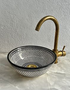 a bowl shaped sink with a gold faucet and metal handles on a marble countertop