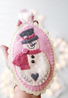 a hand holding up a small felt ornament with a snowman on it