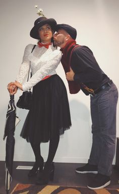 a man standing next to a woman in a dress and top hat holding an umbrella