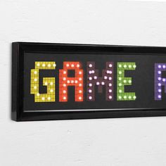 the word game spelled with colored lights on a black framed sign against a white wall