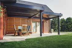 a covered patio with chairs and table in front of a wooden building on the grass