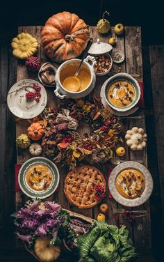 a wooden table topped with plates and bowls filled with food next to pumpkins, gourds and squash