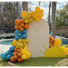 an arch made out of balloons in the shape of sunflowers and flowers on grass next to a swimming pool