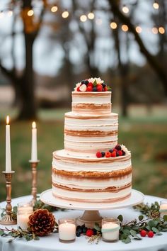 a wedding cake sitting on top of a table next to two lit candles and greenery